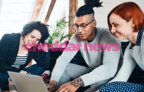 a group of people look at a laptop with the Cheddar News logo superimposed