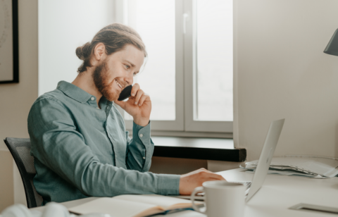 smiling young male talking on the phone and looking at computer